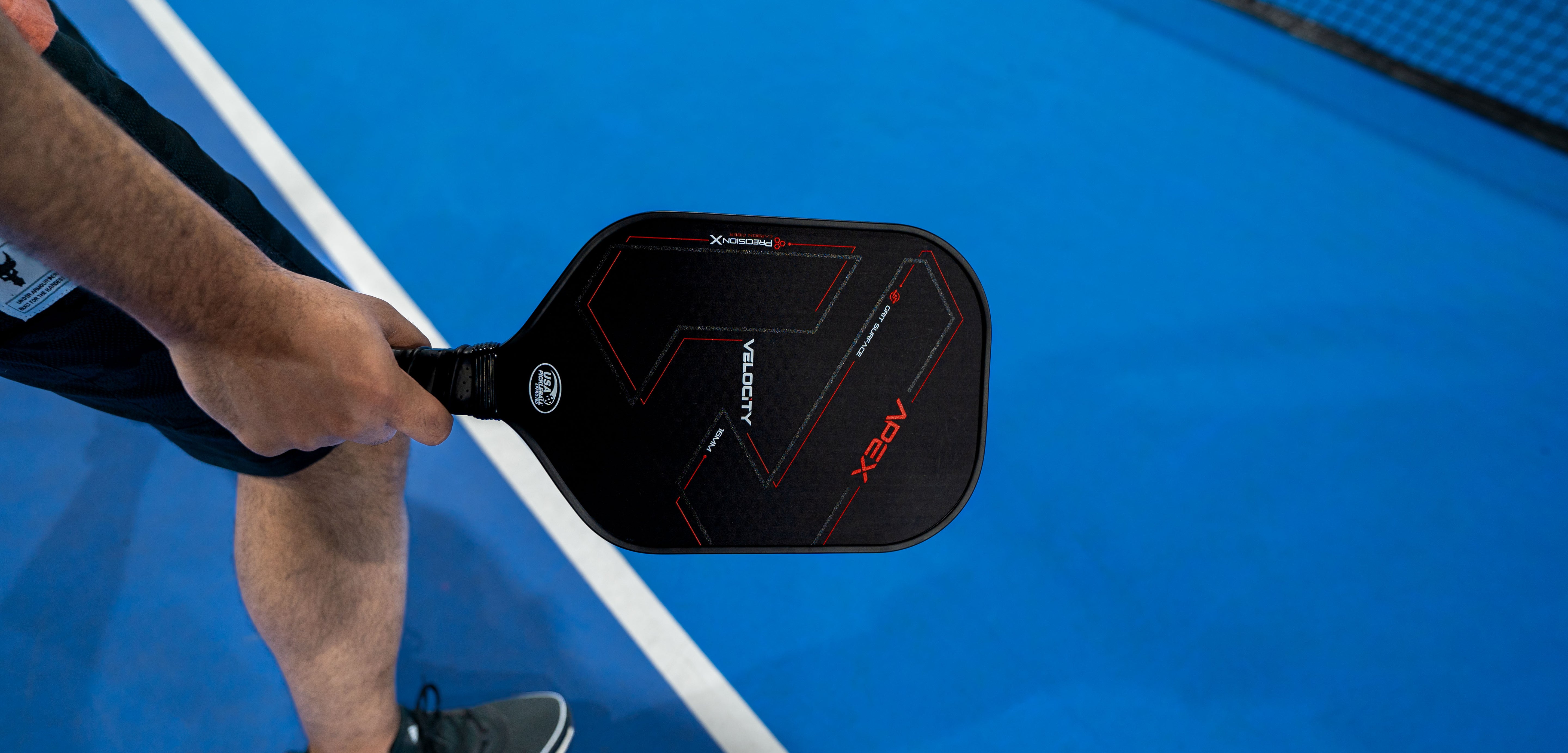 player holding apex pro paddle over a blue pickleball court